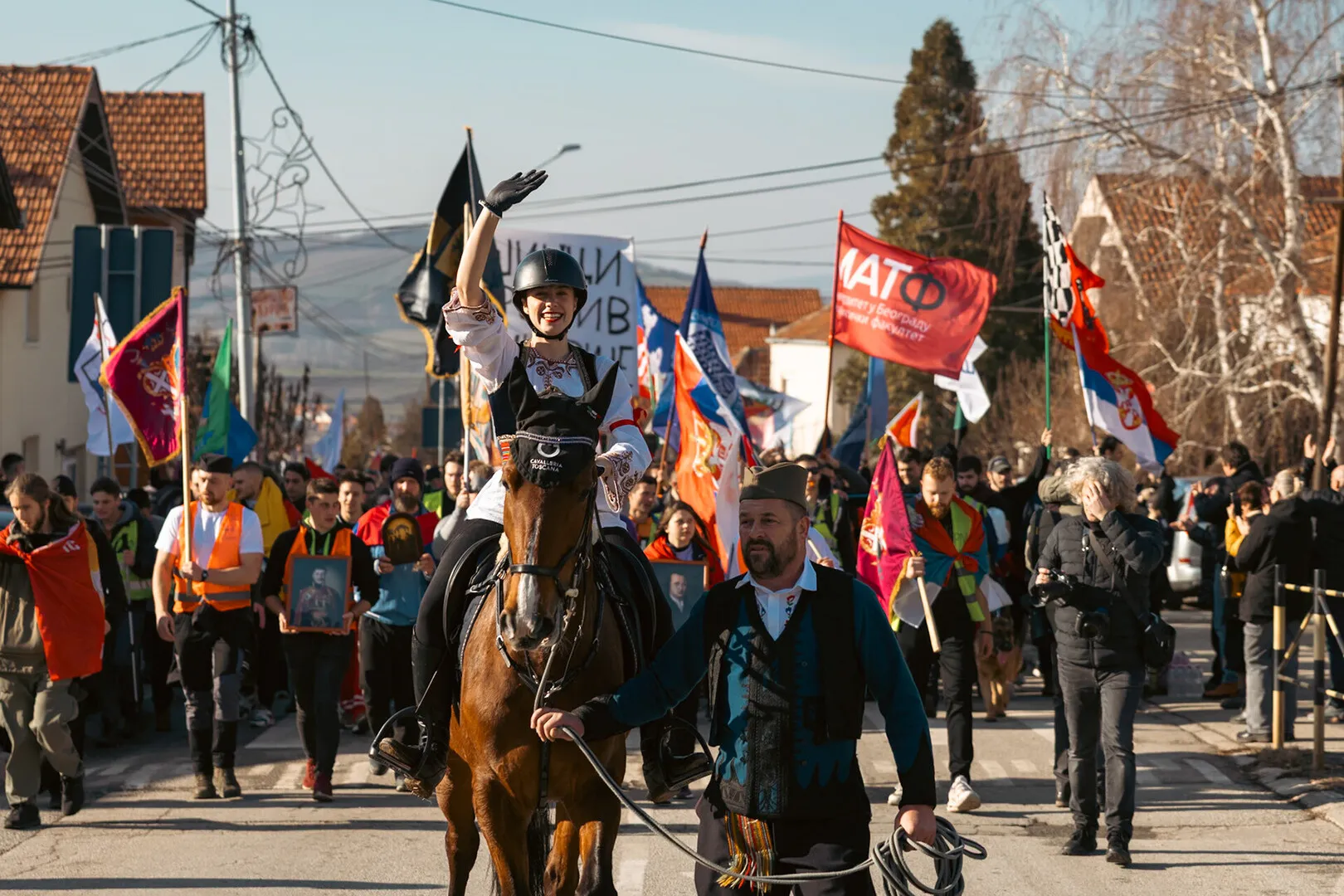 A girl in traditional Serbian attire, riding a horse, leads a line of students.